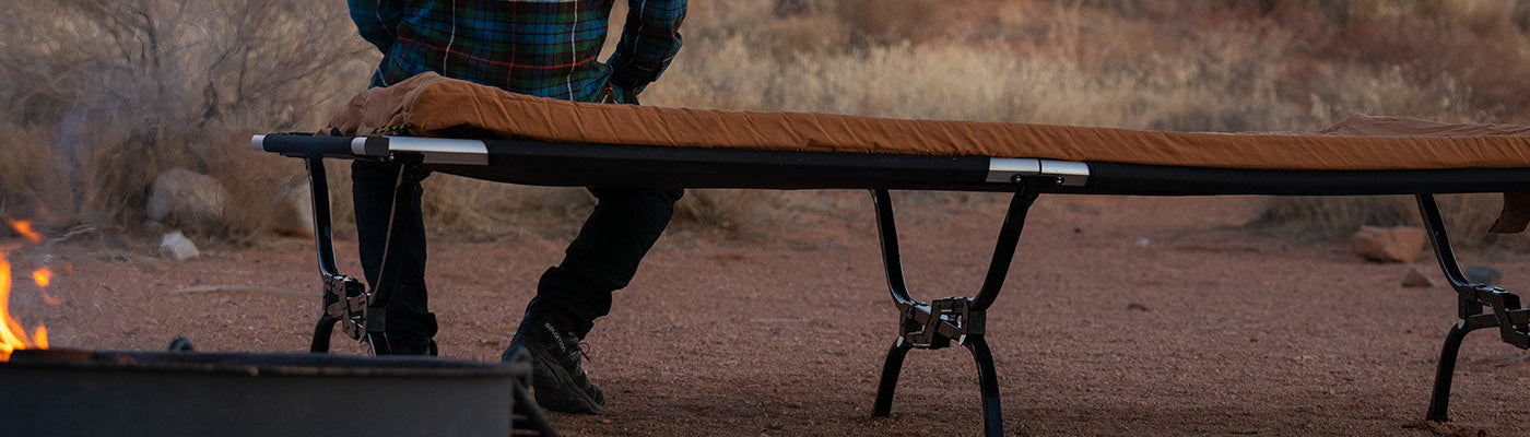 A man sits atop his TETON Sports Outfitter XXL Camp Cot with canvas camp pad.