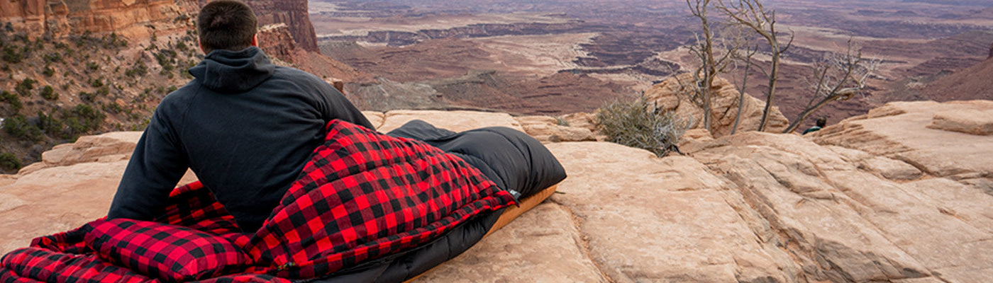 A man sits inside his TETON Sports Celsius XXL Sleeping Bag while viewing a valley below.