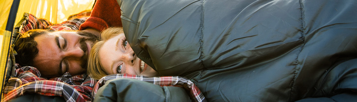 A couple snuggles together inside a TETON Sports Vista Tent while using their Celsius XXL Sleeping Bags.