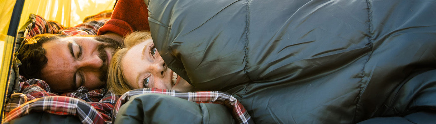 A couple snuggles up in a TETON Sports Mammoth Two-Person Sleeping Bag together.