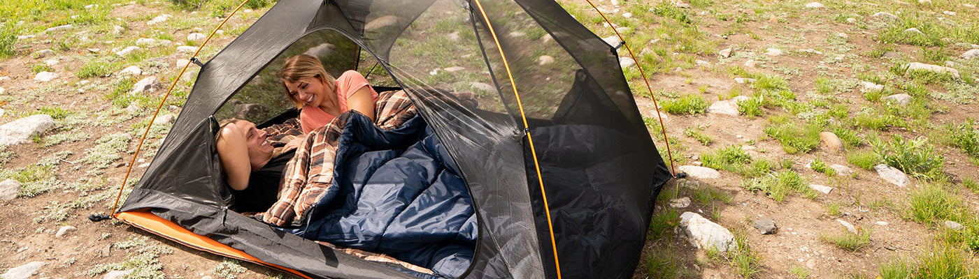 A couple snuggles together inside a TETON Sports Mountain Ultra Tent and their Celsius Sleeping Bags.