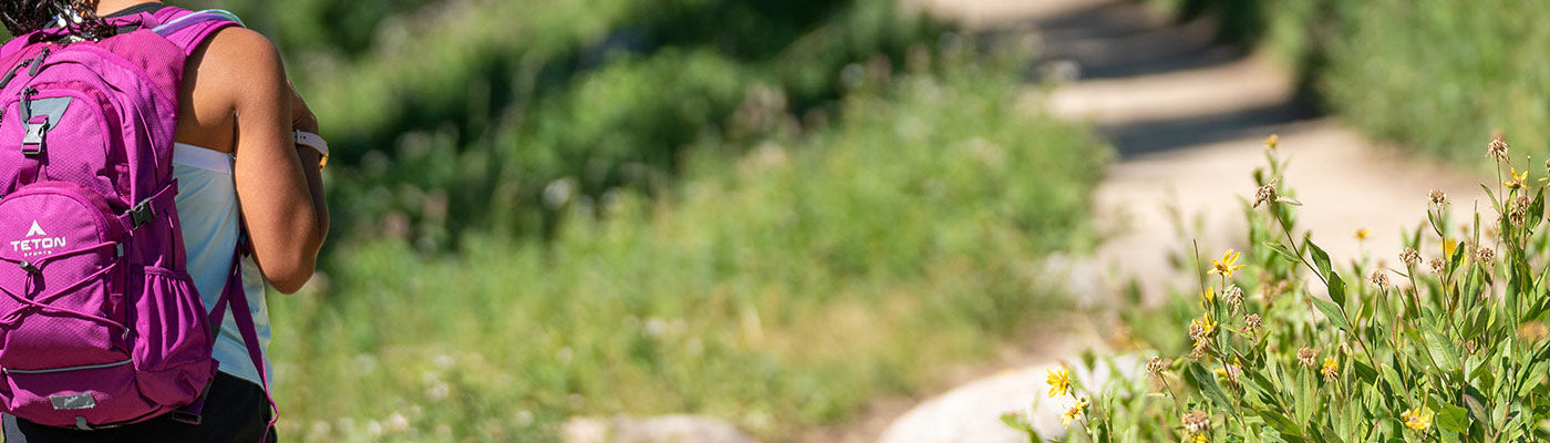 A woman hikes in a field of wildflowers with her TETON Sports Oasis Backpack.