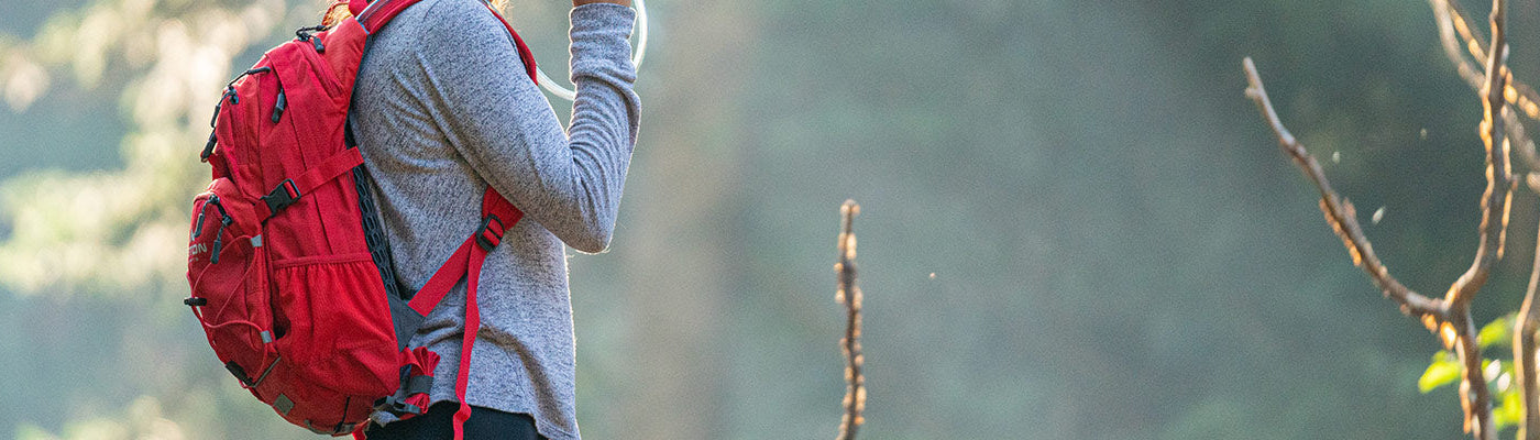 A woman sips from her TETON Sports Oasis Backpack while hiking inside a forest.
