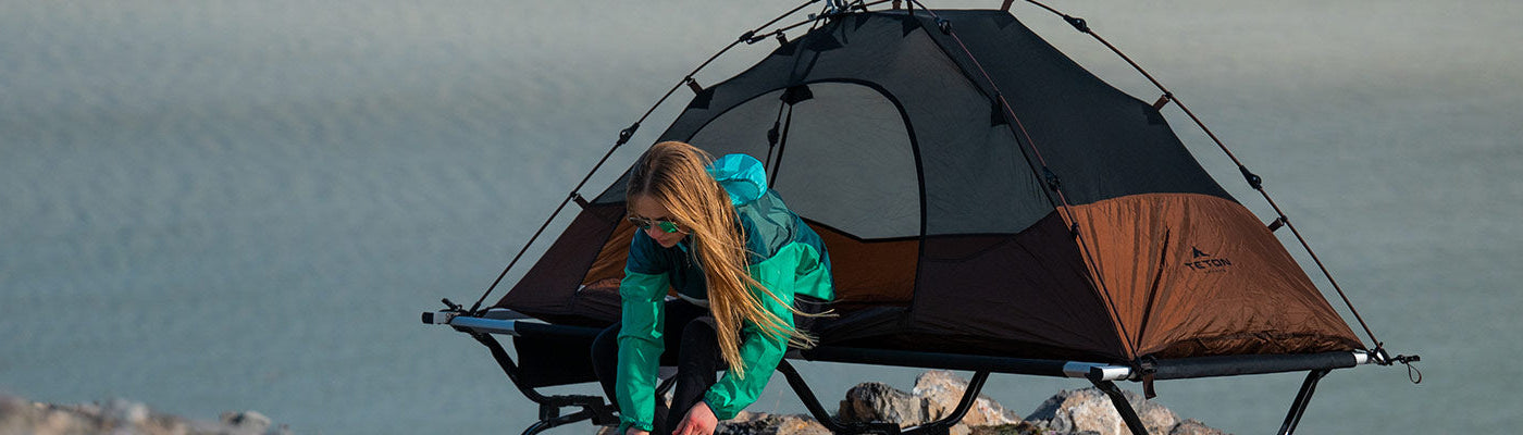 A woman puts on her shoes while leaving her TETON Sports Vista Tent Bundle.