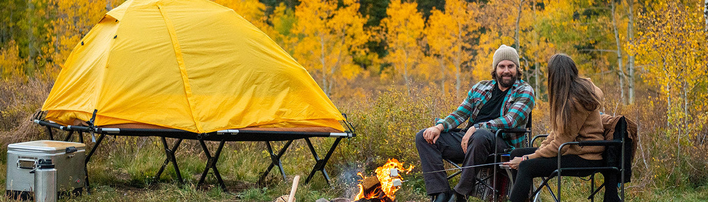 A couple camps togther in a beautiful autumn forest with their TETON Sports Vista Tent Bundle.