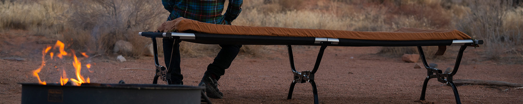 A man sits atop his TETON Sports Outfitter XXL Camp Cot with canvas camp pad.