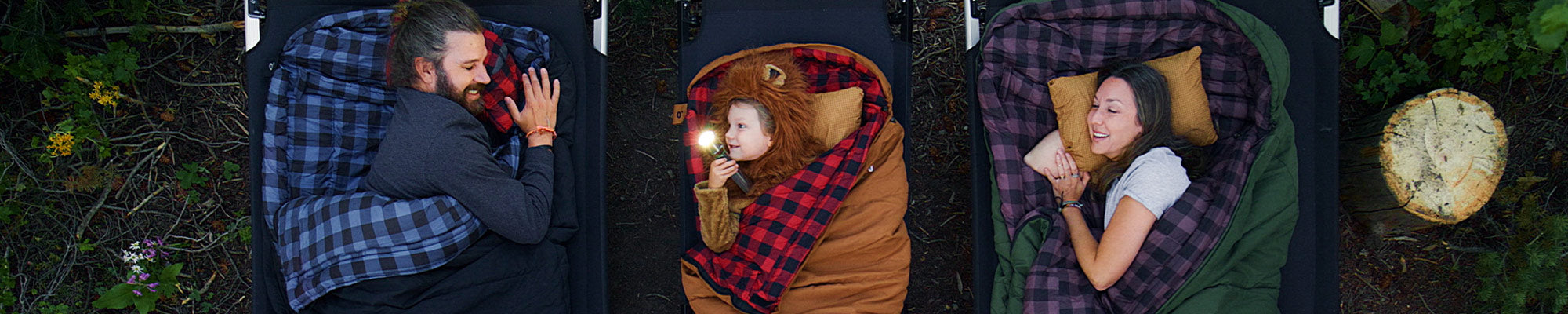 A family shown from above snuggled into their new TETON Sports Bridger Canvas Sleeping Bags in multiple colors and sizes.