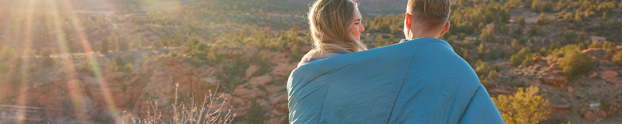 A man and a women sit together beneath a TETON Sports Outdoor Blanket watching the sunset.