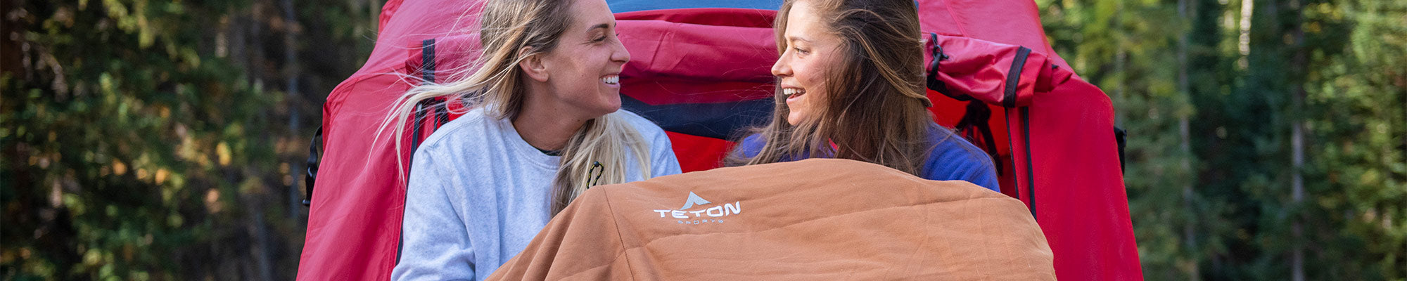 Two women snuggle together in their TETON Sports Canvas Mammoth Sleeping Bag on a cold morning.