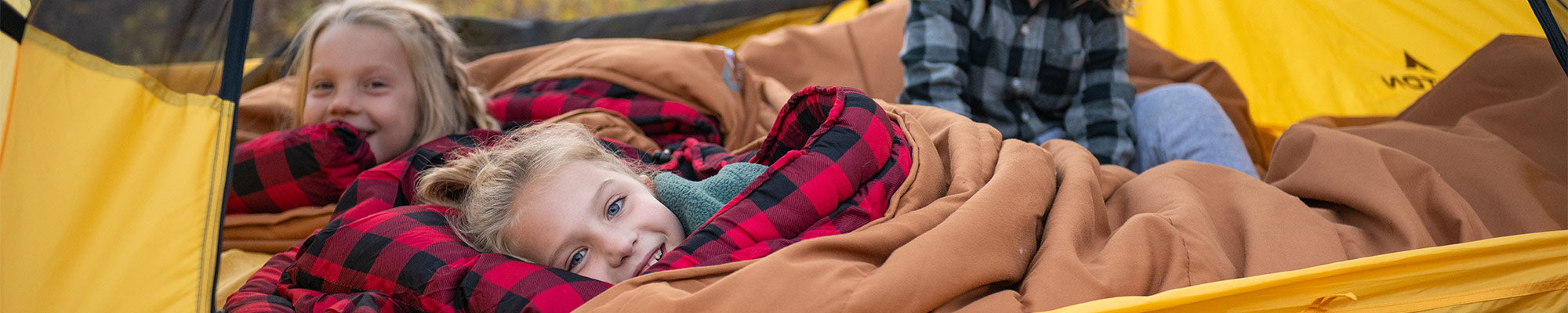 Three children snuggle together in a TETON Sports Vista Tent using their Deer Hunter Canvas Sleeping Bags.