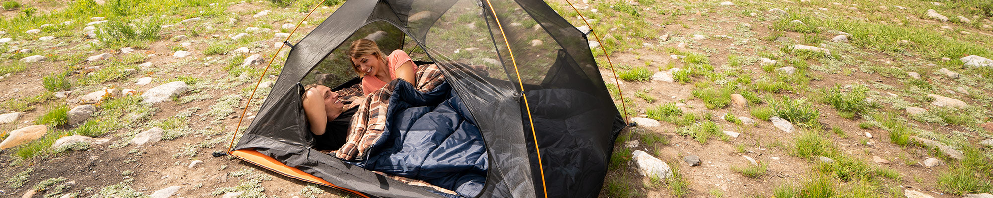 A couple snuggles together inside a TETON Sports Mountain Ultra Tent and their Celsius Sleeping Bags.