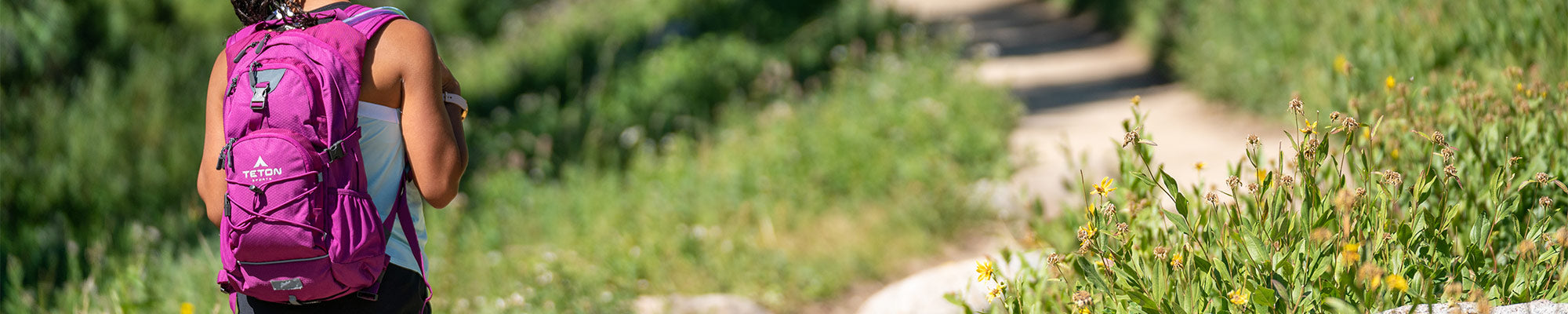 A woman hikes in a field of wildflowers with her TETON Sports Oasis Backpack.