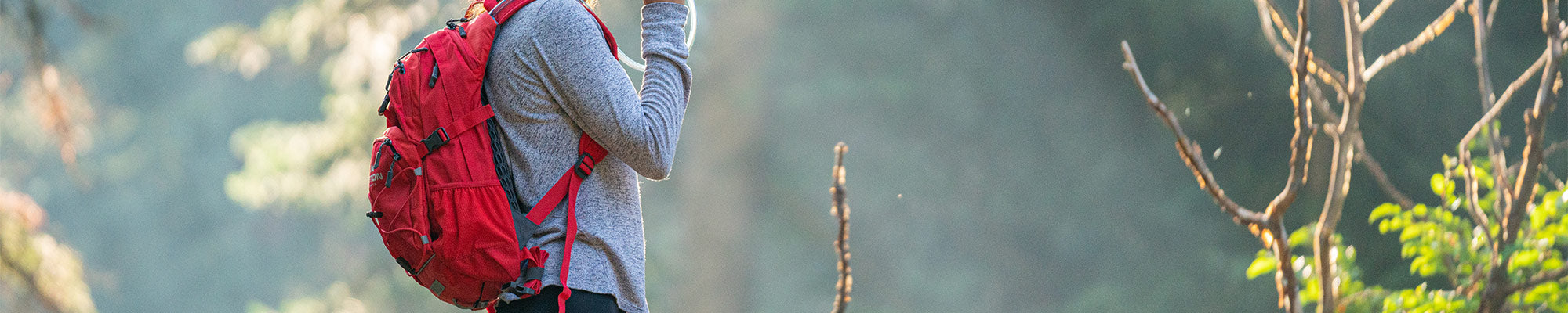 A woman sips from her TETON Sports Oasis Backpack while hiking inside a forest.