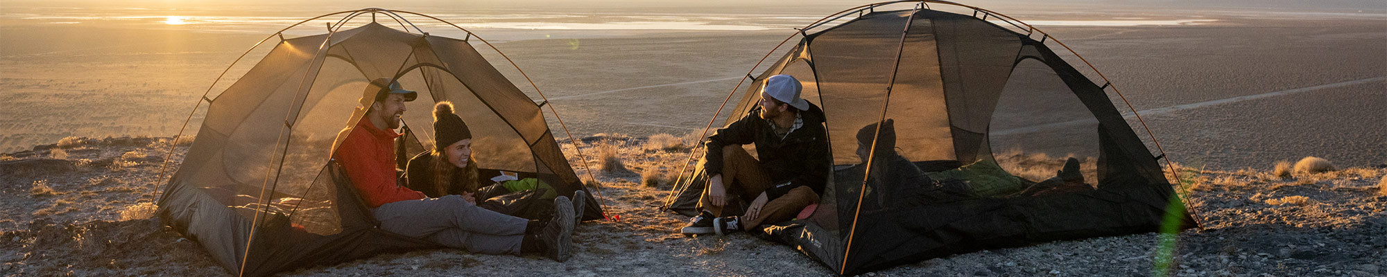 Two couples camp side by side with their matching Mountain Ultra Tents by TETON Sports while the sun sets in the background.