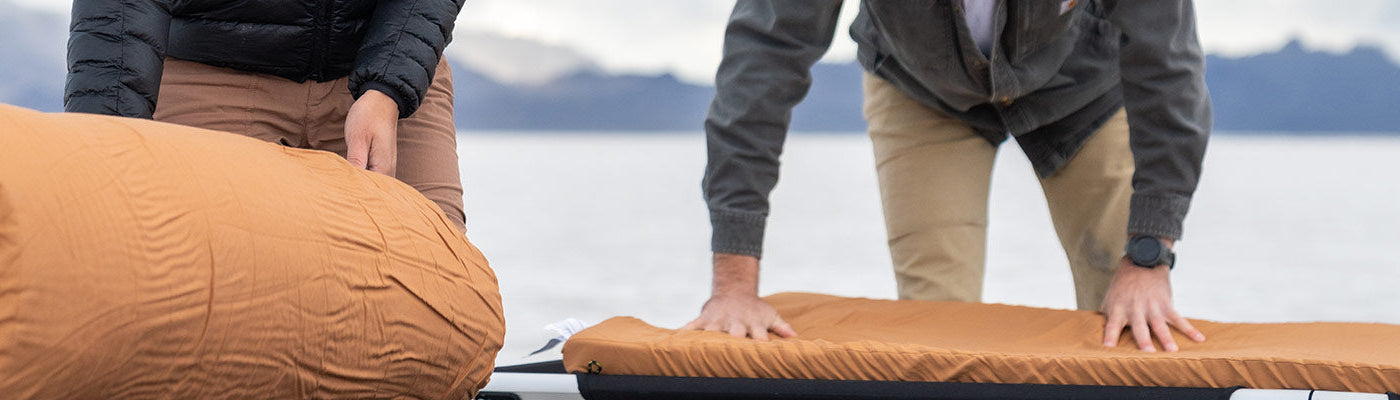 A couple rolls out their TETON Sports canvas camp pads onto their TETON Sports camp cots.