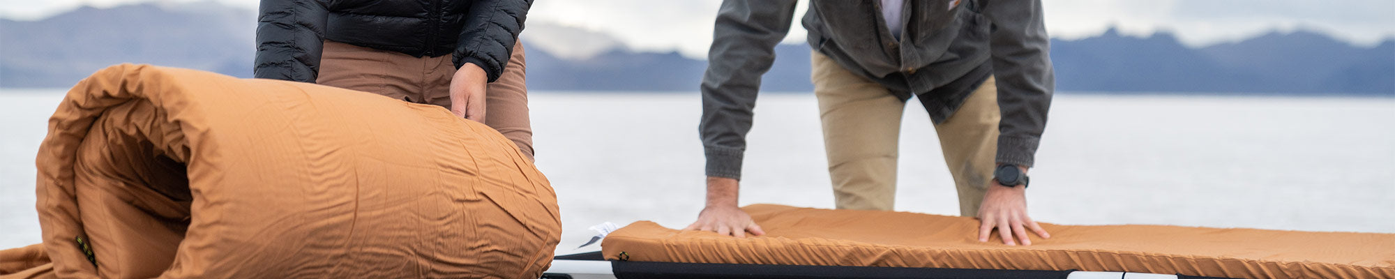 A couple rolls out their TETON Sports canvas camp pads onto their TETON Sports camp cots.