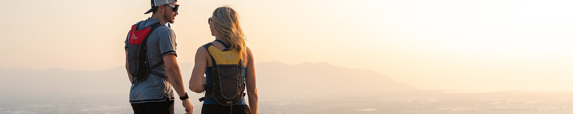 Two runners stop to sip from their TETON Sports TrailRunner 2L Hydration Packs while viewing a city from above.