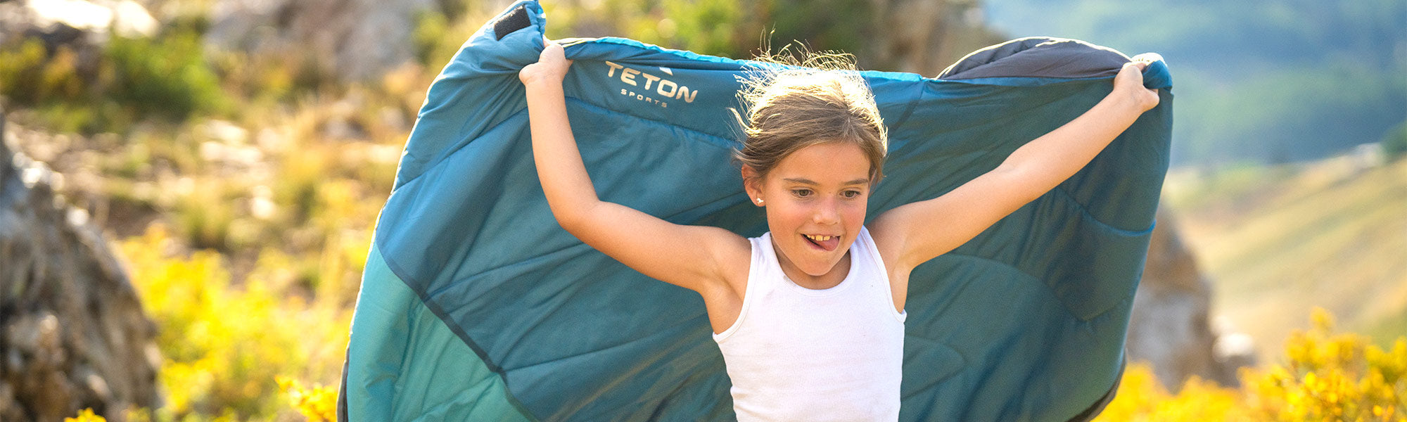 A little girl holds a new Li'l Celsius Kids' Sleeping Bag while running through a meadow