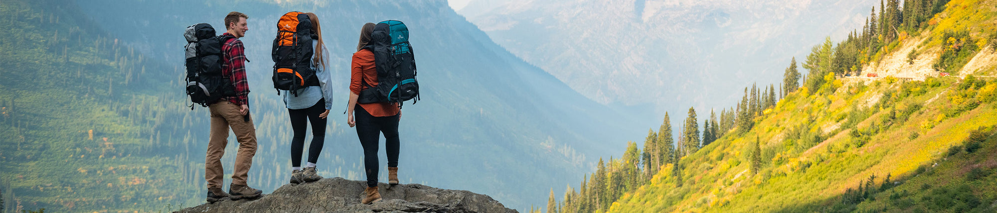 TETON Story & Values: Image shows three backpackers standing atop a large boulder. They are wearing TETON Sports backpacks and are staring away from the camera at a large mountain in the distance.